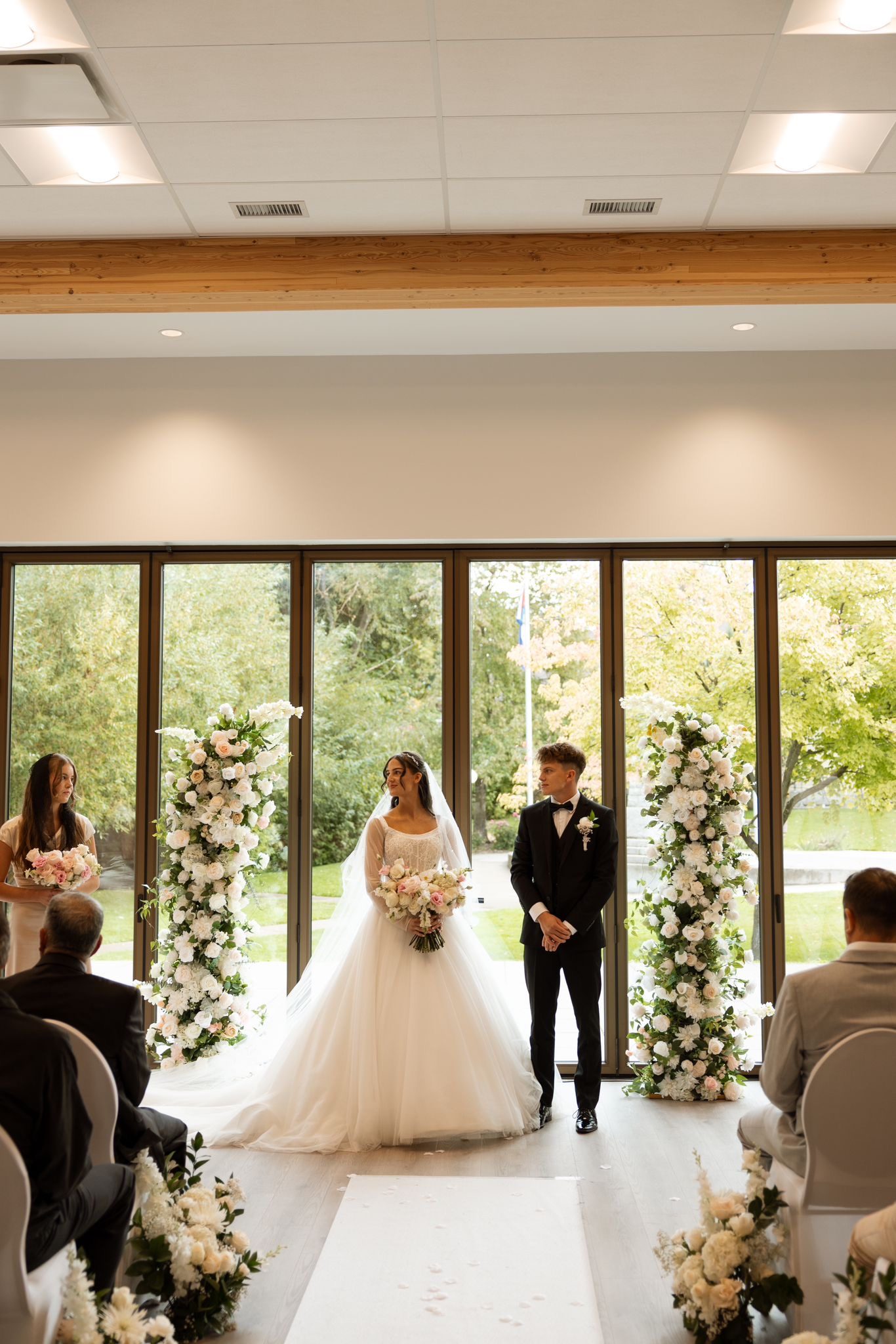 Bride and groom at the altar between two lush white and blush faux floral pillars by Kelowna Wedding Arches, at a real ceremony in an Okanagan venue